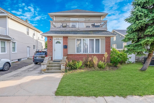 view of front facade with a balcony, concrete driveway, brick siding, roof with shingles, and a front yard