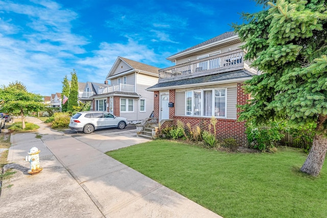 view of front of house featuring a front lawn, brick siding, and a balcony