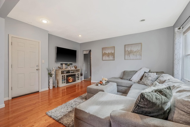 living room featuring a glass covered fireplace, baseboards, recessed lighting, and light wood-style floors