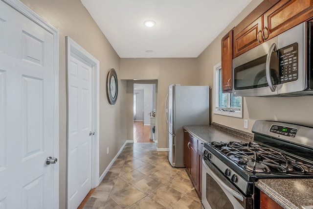 kitchen featuring dark countertops, baseboards, brown cabinetry, and appliances with stainless steel finishes