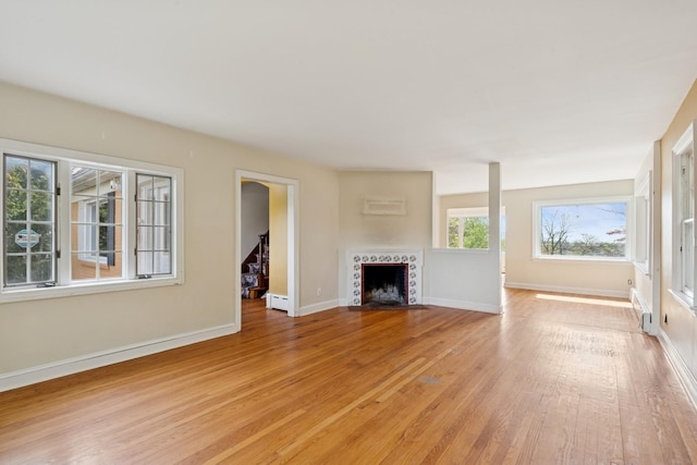 unfurnished living room featuring a tiled fireplace, light wood-style flooring, baseboard heating, and baseboards