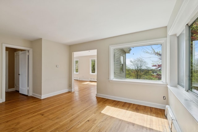spare room with baseboards, light wood-style flooring, and a baseboard radiator