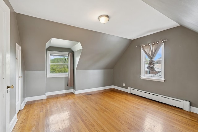 additional living space with arched walkways, a baseboard radiator, light wood-style floors, baseboards, and lofted ceiling