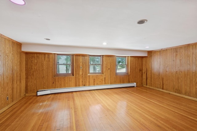 empty room featuring a healthy amount of sunlight, hardwood / wood-style flooring, a baseboard heating unit, and wooden walls