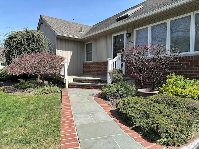 doorway to property with brick siding, a yard, and a shingled roof