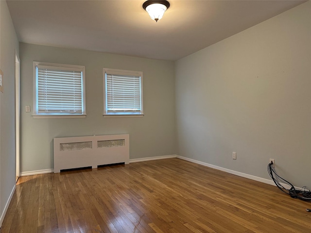 spare room featuring wood-type flooring, radiator, and baseboards