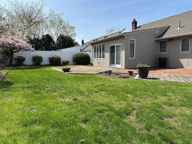 rear view of property featuring a chimney, fence, a yard, a patio, and roof with shingles