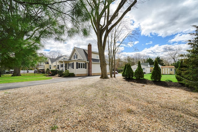 view of front of house featuring a chimney, fence, an outbuilding, driveway, and a front lawn