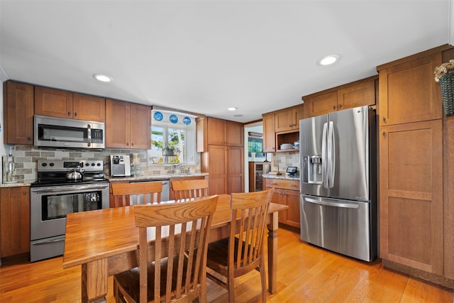 kitchen featuring recessed lighting, stainless steel appliances, decorative backsplash, brown cabinetry, and light wood-style flooring