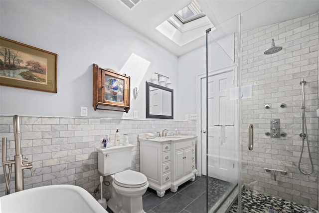 full bath with a skylight, tile patterned floors, tile walls, vanity, and a stall shower