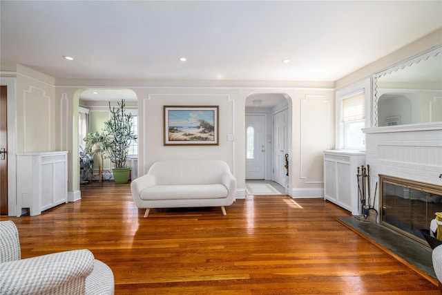 living area with a brick fireplace, wood finished floors, and arched walkways
