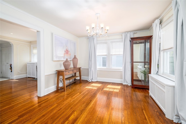 dining area with plenty of natural light, wood-type flooring, arched walkways, and an inviting chandelier