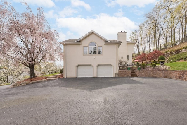 view of home's exterior with a garage, a chimney, driveway, and stucco siding