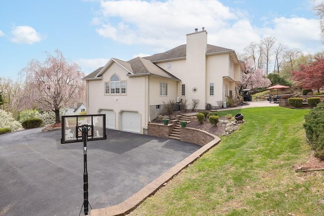 view of side of home featuring a lawn, a chimney, an attached garage, and driveway