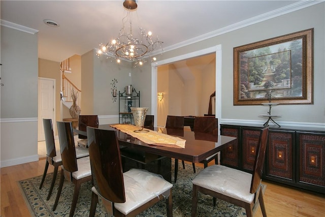 dining area featuring an inviting chandelier, ornamental molding, light wood finished floors, and stairway