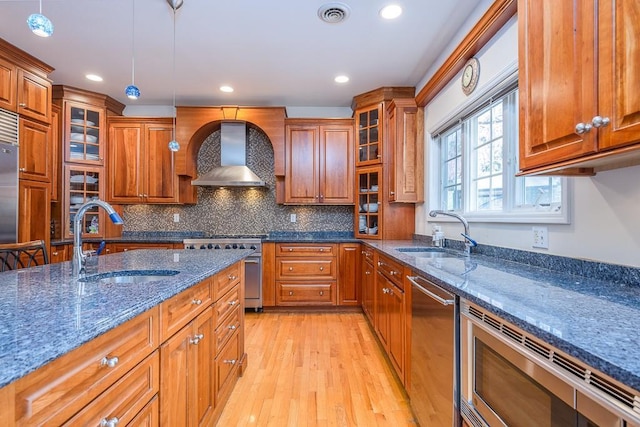 kitchen featuring brown cabinets, stainless steel appliances, a sink, and wall chimney exhaust hood