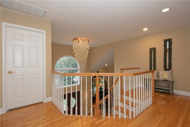 hallway featuring a notable chandelier, visible vents, wood finished floors, and an upstairs landing