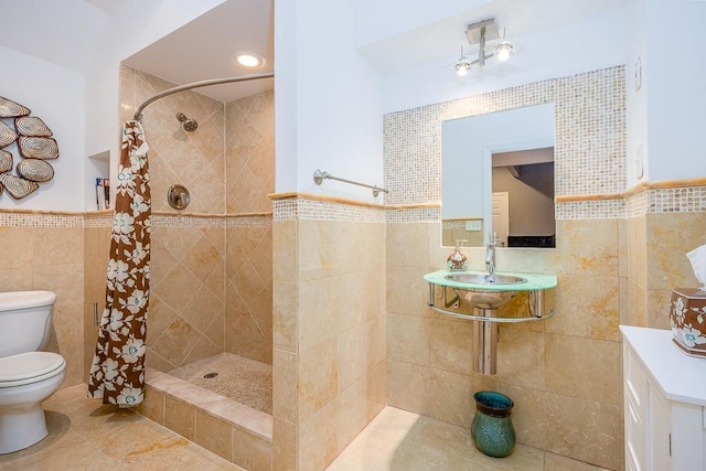 bathroom featuring tile patterned flooring, toilet, tile walls, a wainscoted wall, and a tile shower