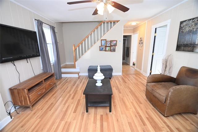 living area featuring baseboards, light wood-style floors, a ceiling fan, stairway, and crown molding