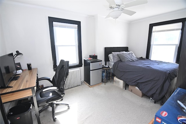 carpeted bedroom featuring radiator heating unit, freestanding refrigerator, ornamental molding, and multiple windows