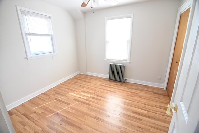spare room with radiator, light wood-style floors, ceiling fan, and plenty of natural light