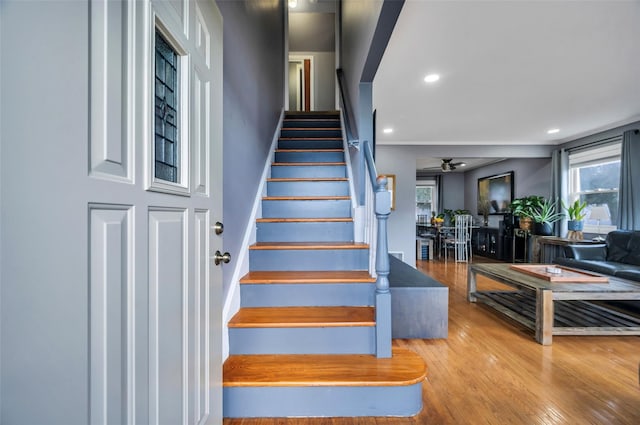 stairway featuring wood finished floors, a healthy amount of sunlight, and ceiling fan