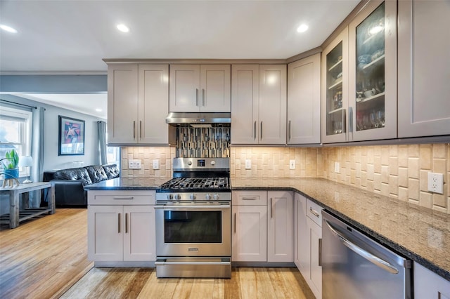 kitchen featuring under cabinet range hood, appliances with stainless steel finishes, dark stone counters, and light wood-style floors