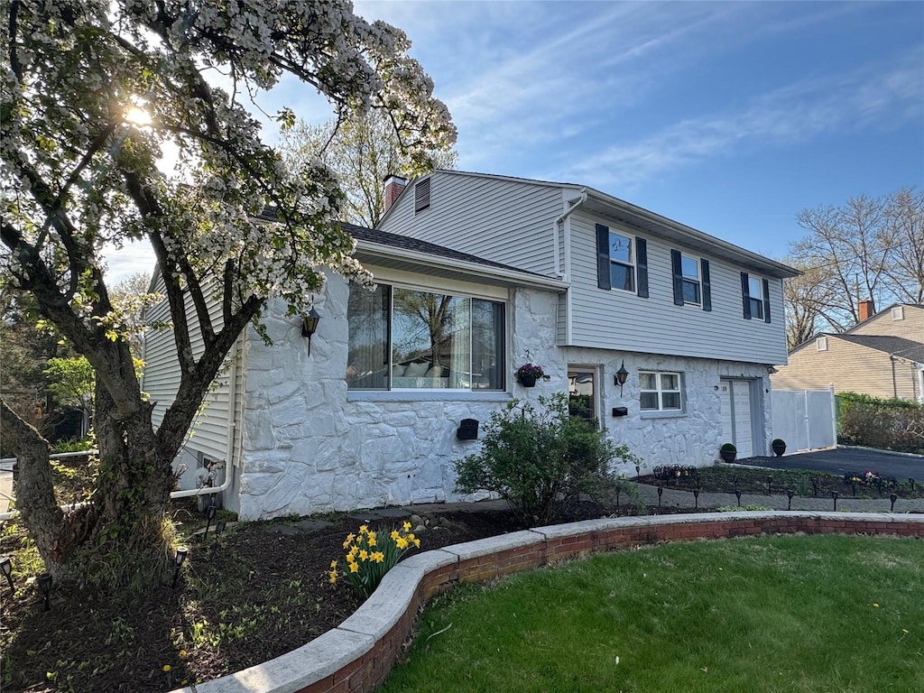 tri-level home featuring a chimney, a front yard, and stone siding