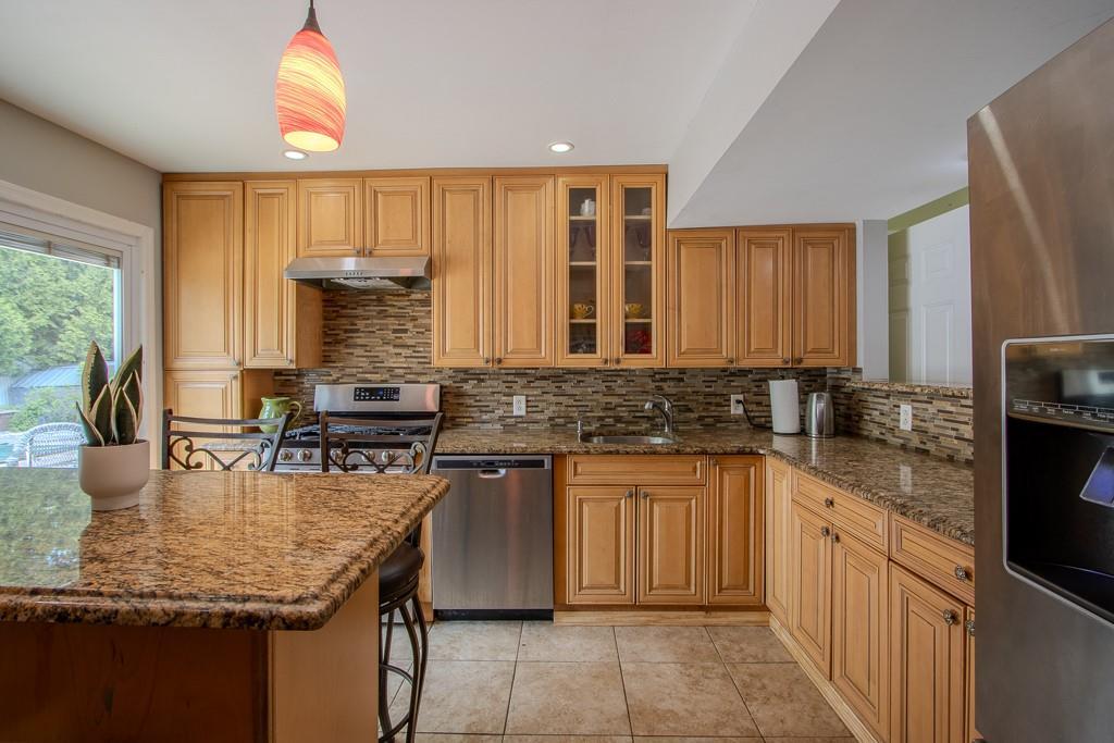 kitchen featuring appliances with stainless steel finishes, tasteful backsplash, a sink, under cabinet range hood, and light tile patterned flooring