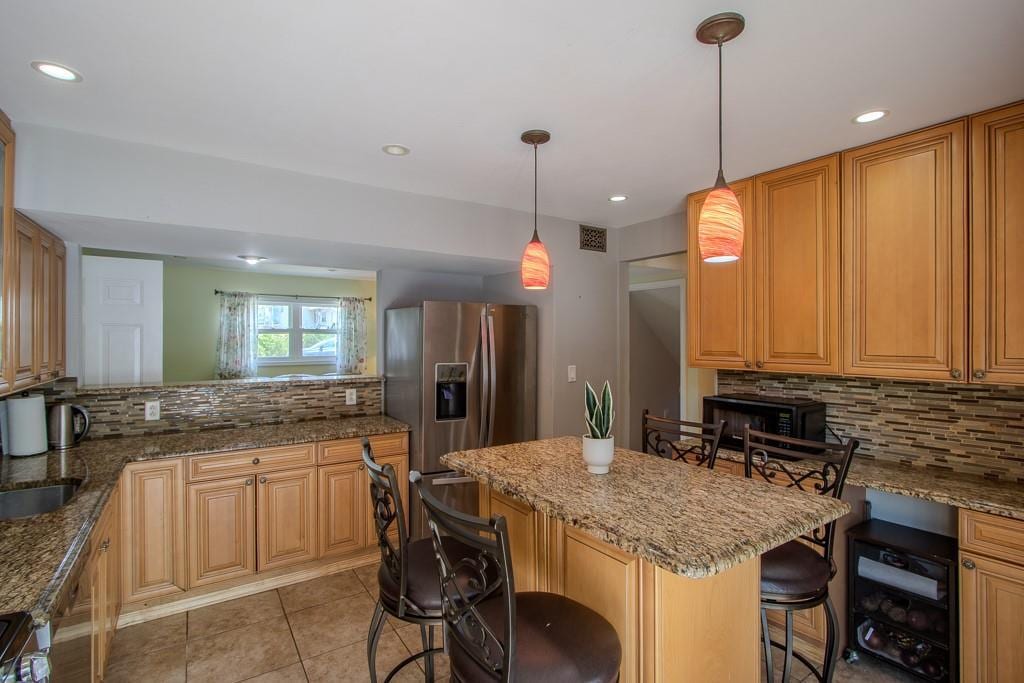 kitchen with a breakfast bar area, a kitchen island, backsplash, stainless steel refrigerator with ice dispenser, and wine cooler