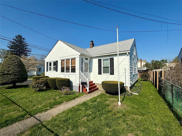 back of house with a chimney, fence, entry steps, a yard, and roof with shingles