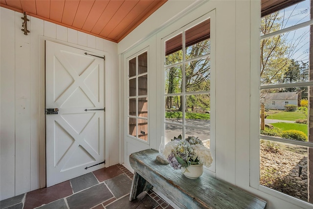 doorway to outside featuring stone tile floors, a healthy amount of sunlight, and wooden ceiling