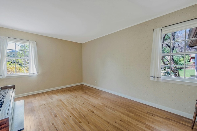 spare room featuring light wood-style floors, crown molding, and baseboards