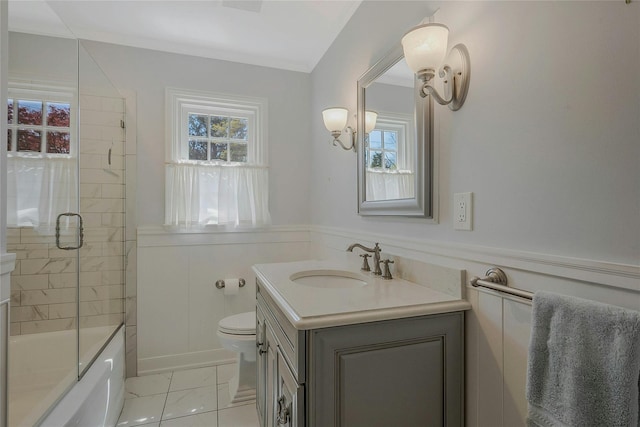 bathroom with vanity, toilet, a wainscoted wall, and shower / bath combination with glass door