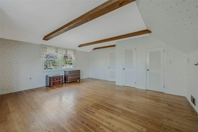 unfurnished living room with lofted ceiling with beams, wallpapered walls, and hardwood / wood-style flooring