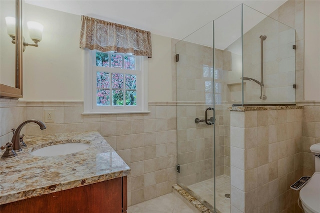 bathroom with a shower stall, tile walls, a wainscoted wall, toilet, and vanity