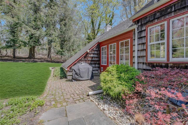exterior space with a lawn, roof with shingles, a patio, and a chimney