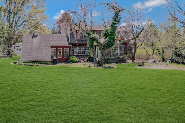 back of property featuring a chimney, french doors, roof with shingles, and a lawn