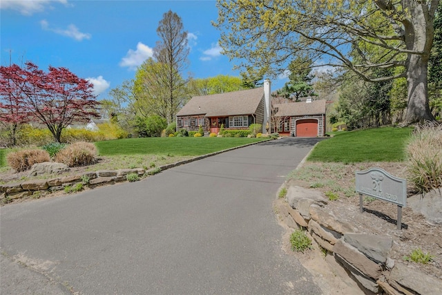 view of front of home featuring a chimney, aphalt driveway, a front lawn, and an attached garage