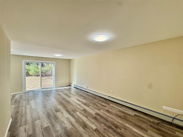 unfurnished room with a baseboard heating unit, baseboards, and wood finished floors