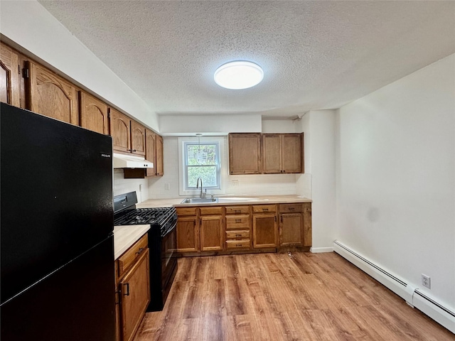kitchen featuring light wood finished floors, under cabinet range hood, a sink, black appliances, and baseboard heating