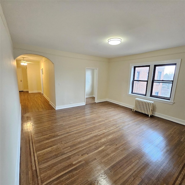 spare room featuring baseboards, arched walkways, radiator heating unit, and dark wood-style floors