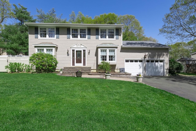 colonial-style house with a garage, fence, driveway, and a front lawn