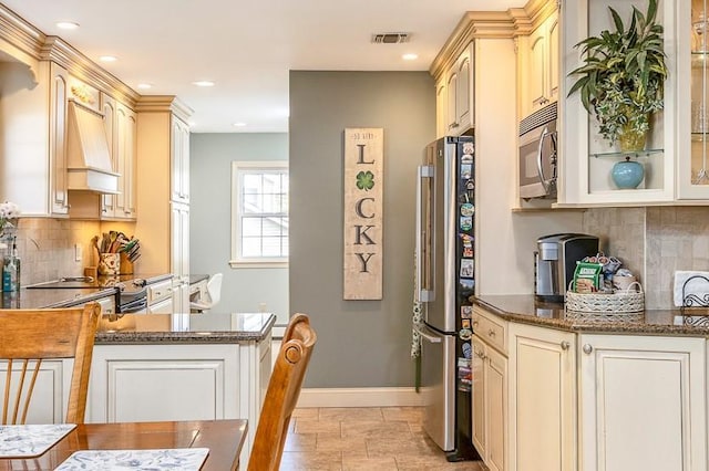 kitchen with appliances with stainless steel finishes, dark stone counters, baseboards, backsplash, and custom exhaust hood