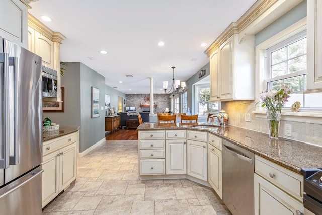 kitchen with backsplash, a sink, an inviting chandelier, stainless steel appliances, and cream cabinetry