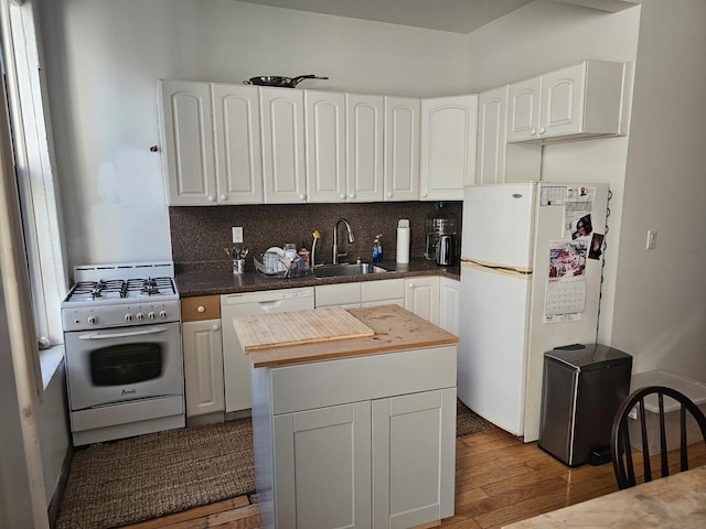 kitchen featuring white cabinets, a sink, tasteful backsplash, wood finished floors, and white appliances
