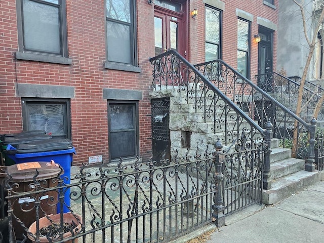 view of exterior entry with fence and brick siding