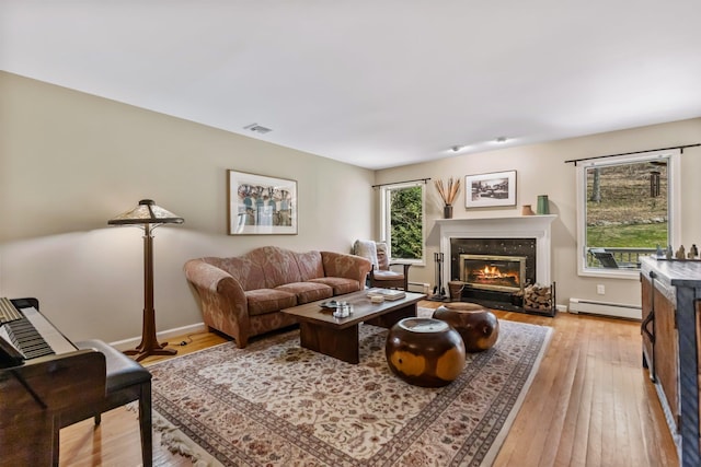 living area featuring baseboard heating, baseboards, a high end fireplace, and light wood-style flooring