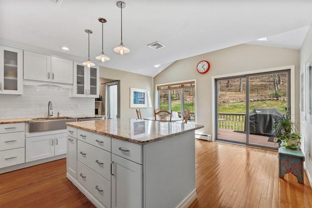 kitchen with a sink, tasteful backsplash, visible vents, light wood-style flooring, and vaulted ceiling