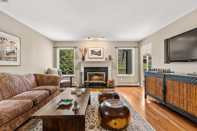 living area with wood finished floors, a baseboard heating unit, and a high end fireplace